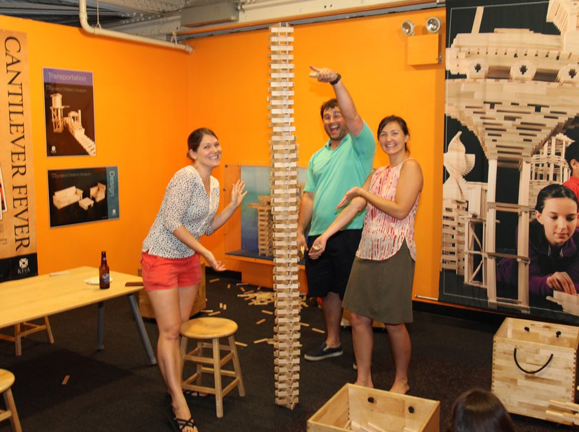 Three adults playing with KEVA planks during an evening at the Museum